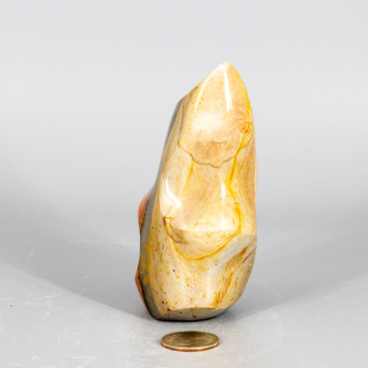 Decorative polychrome jasper flame stone with a coin for scale on a light gray background