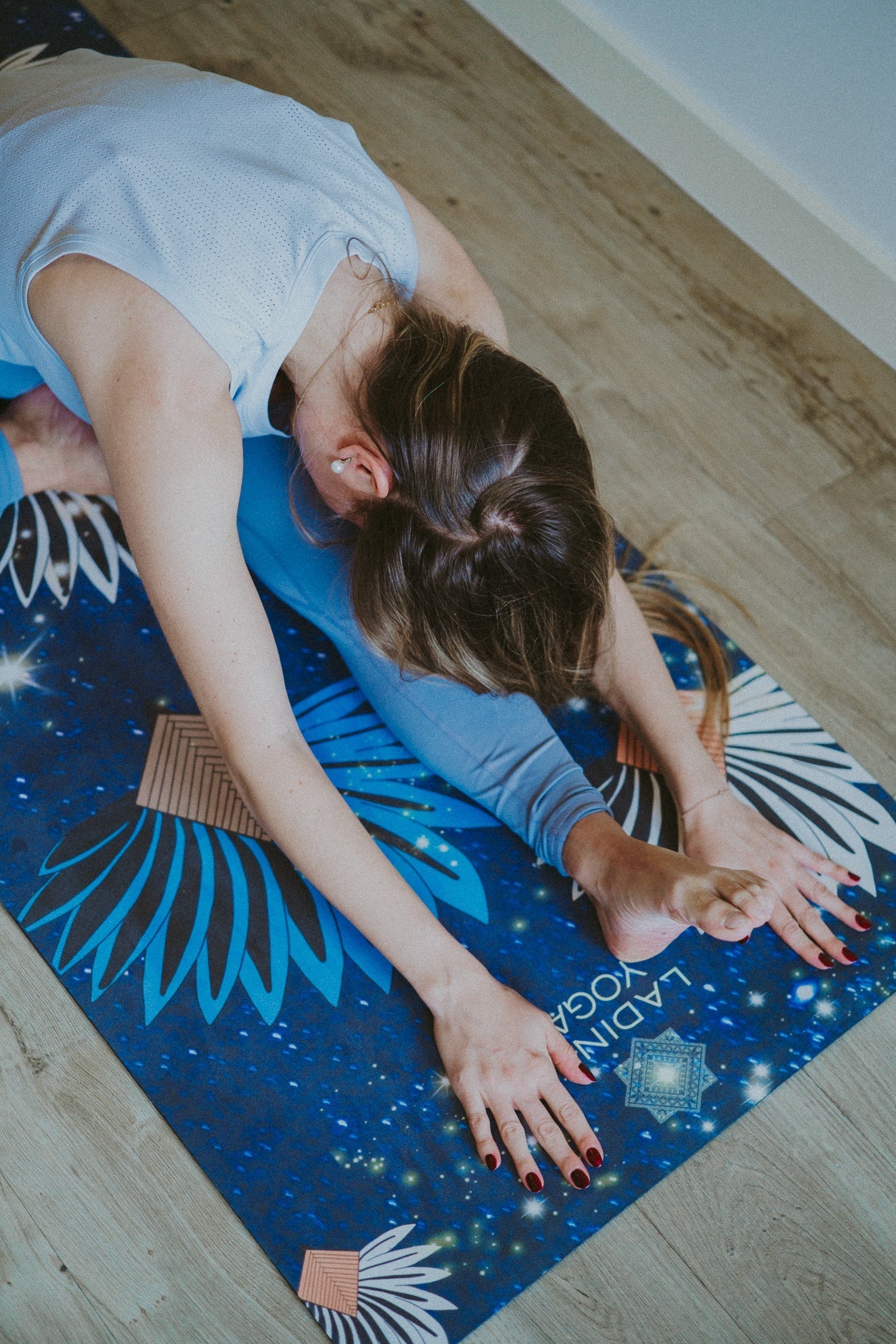 Person stretching on a blue yoga mat with star and moon designs on a wooden floor.