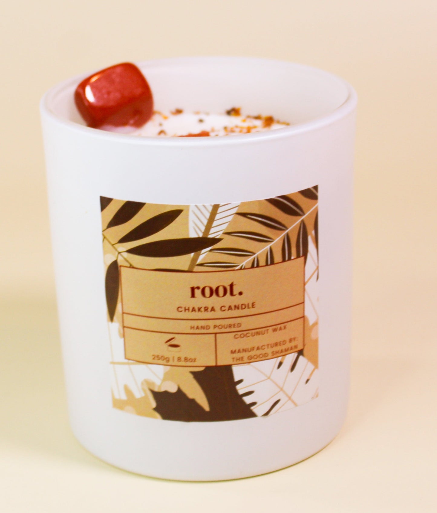 White root chakra candle with a label featuring leaf designs on a beige background