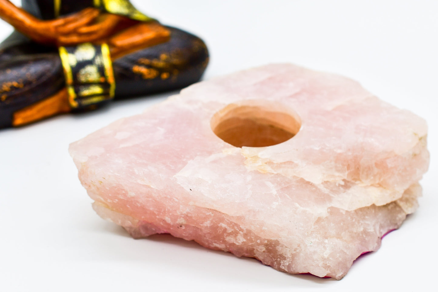 Rose quartz candle holder on a white surface with a decorative item in the background