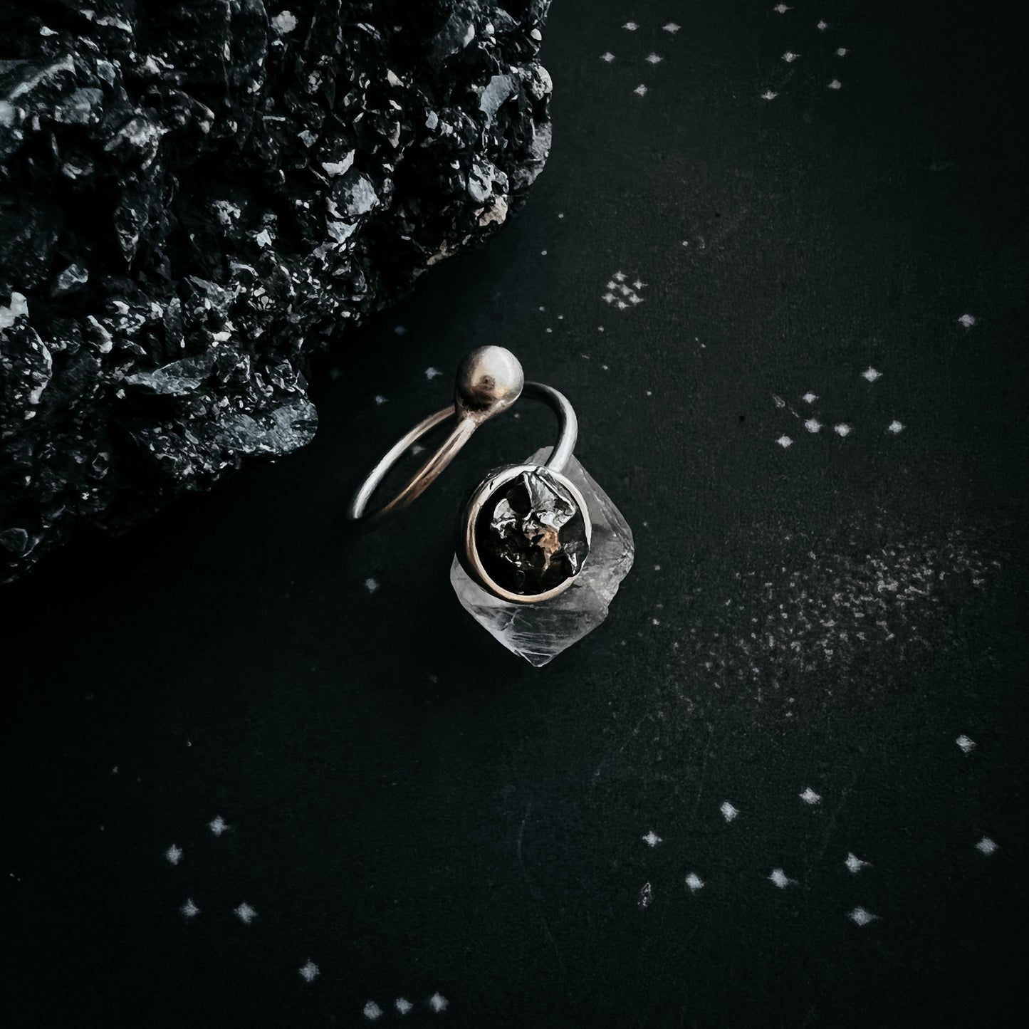 Silver meteorite ring with a circular design on a dark textured surface