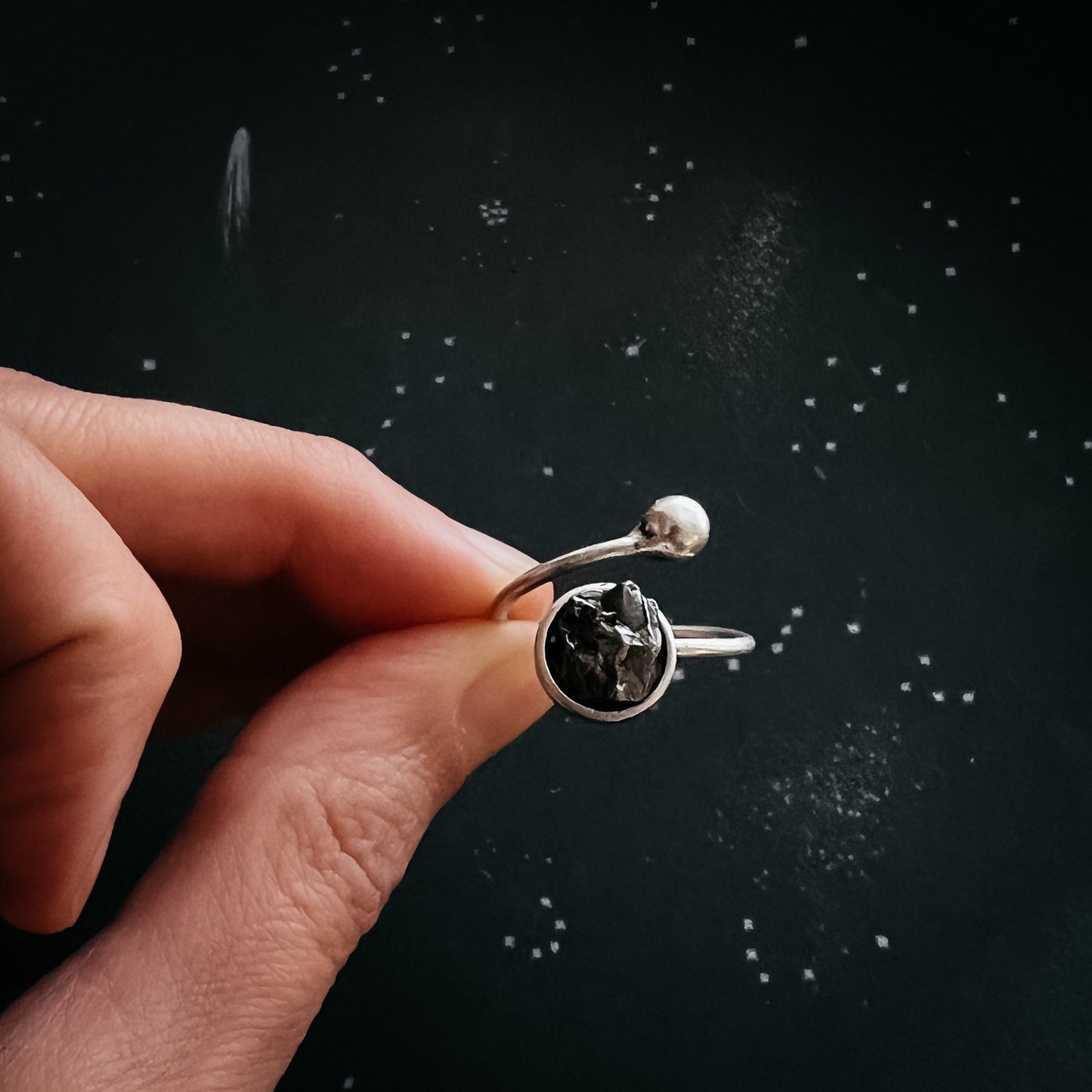 Silver ring with meteorite held by a hand against a dark background