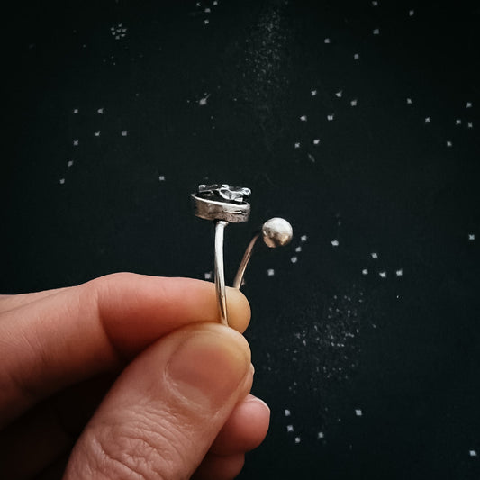 Adjustable silver ring with meteorite held between two fingers against a dark background