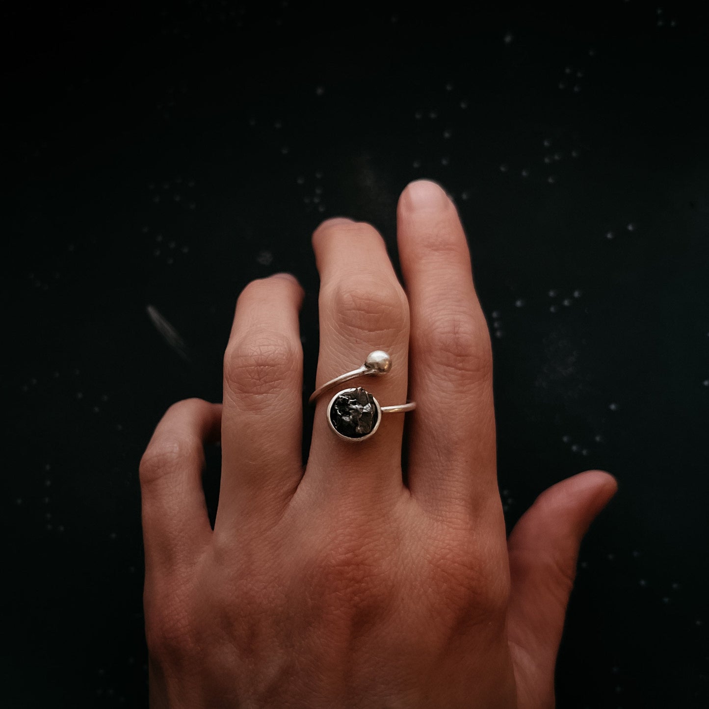 Hand wearing a ring with meteorite on a black background