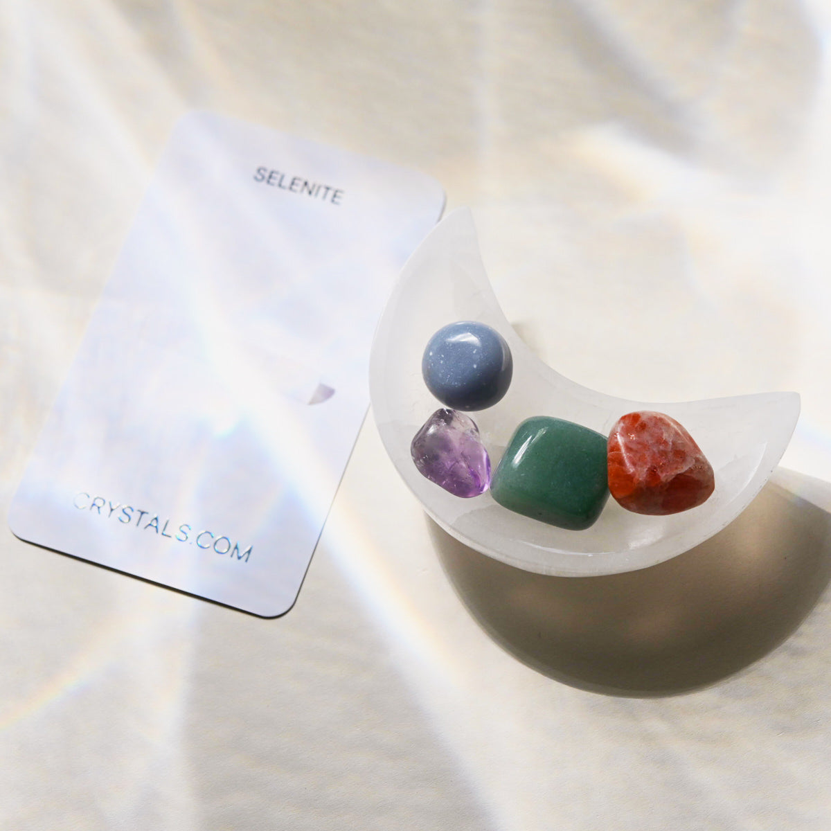 Set of colorful crystals in a selenite container with a branded card on a light background