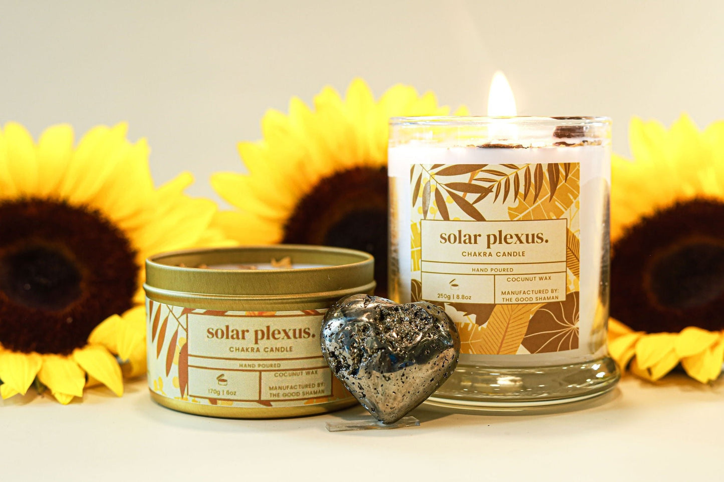 Two candles labeled 'solar plexus' with sunflowers in the background on a light surface.