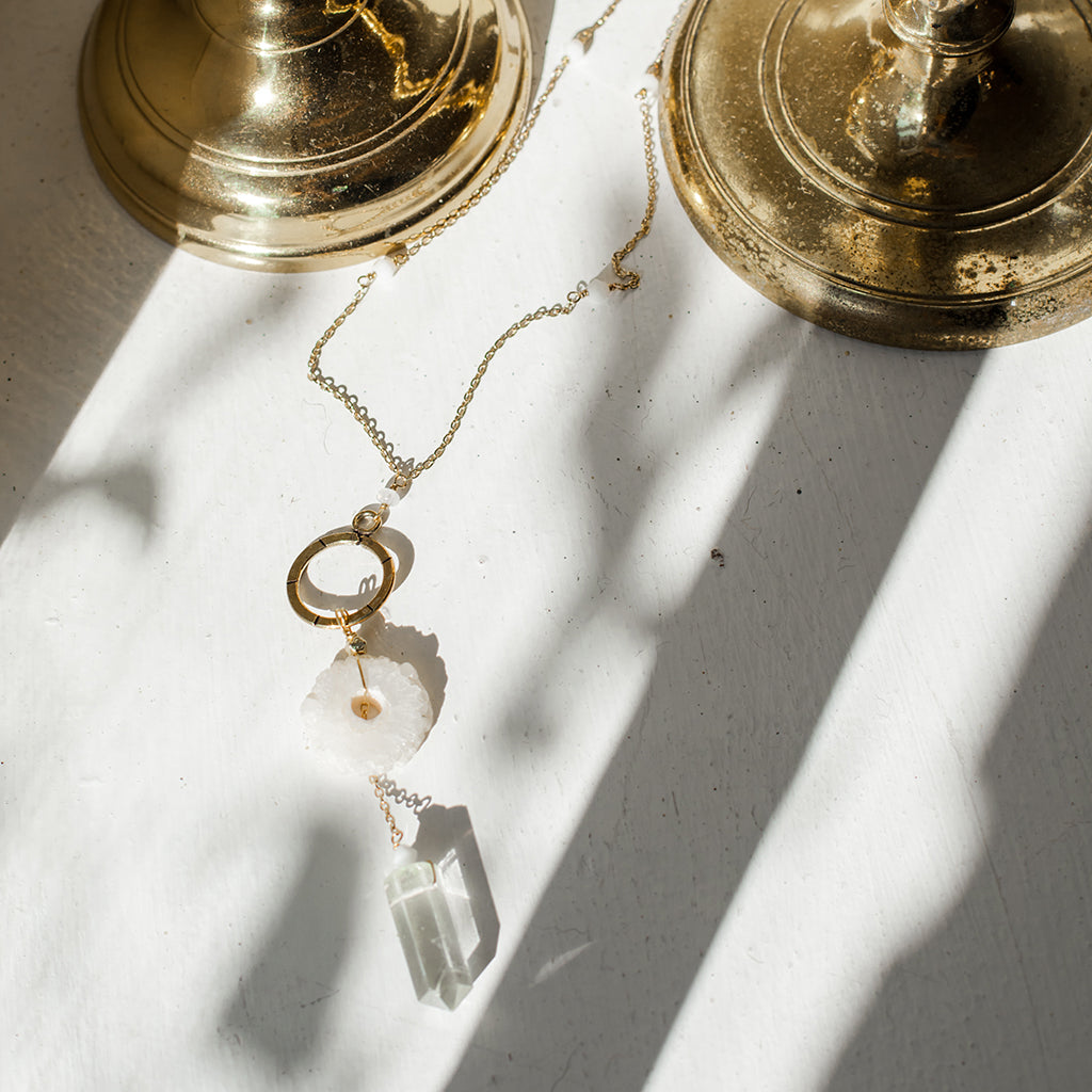Gold necklace with crystal pendant on a white surface