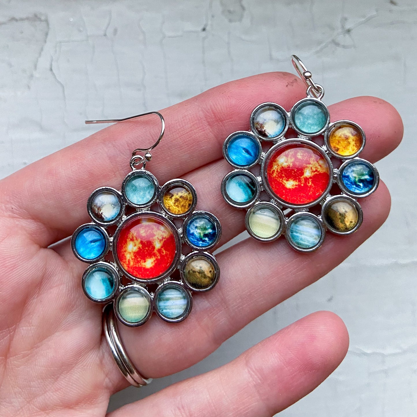 Colorful celestial-themed earrings held in a hand against a light background