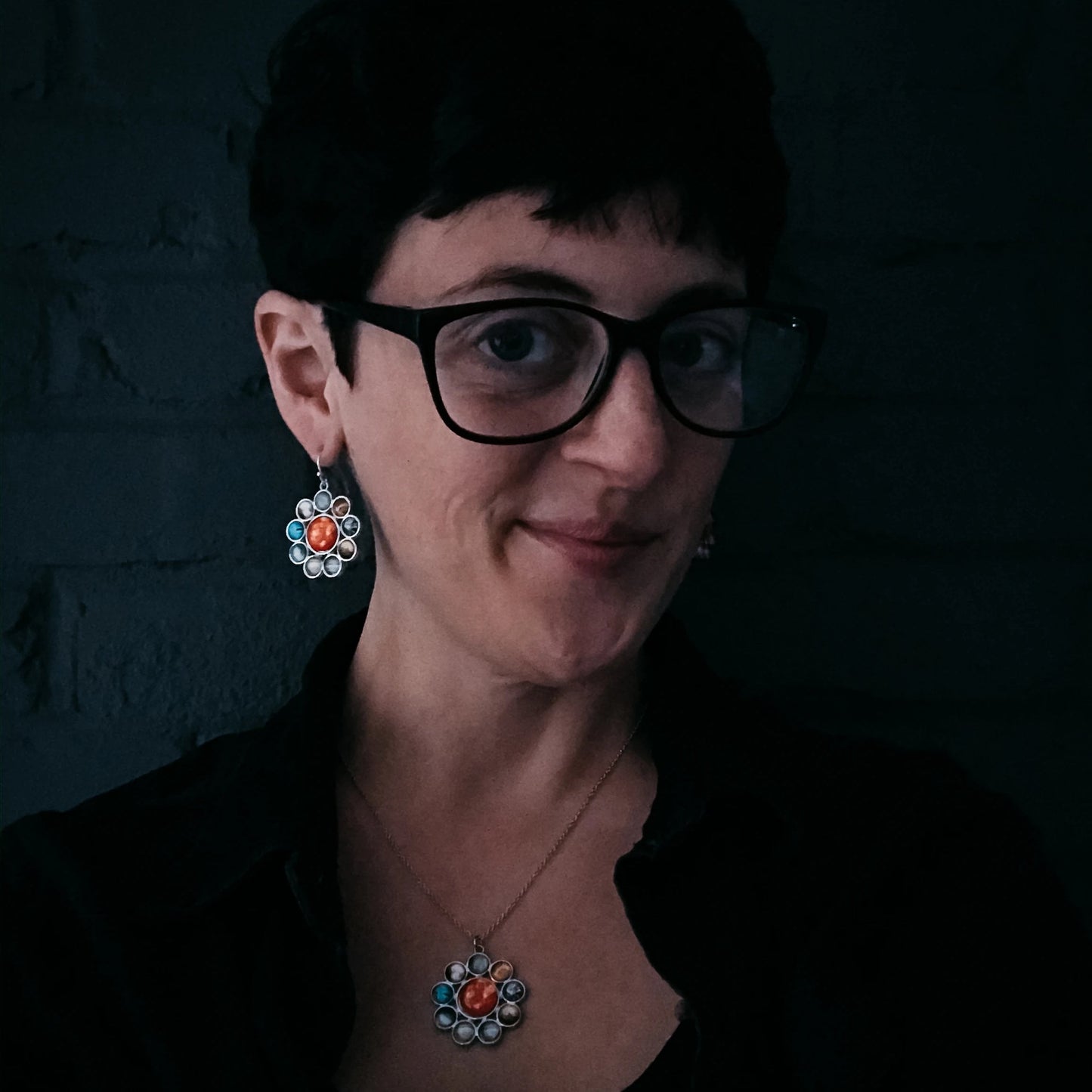 Woman wearing glasses and colorful earrings against a dark background