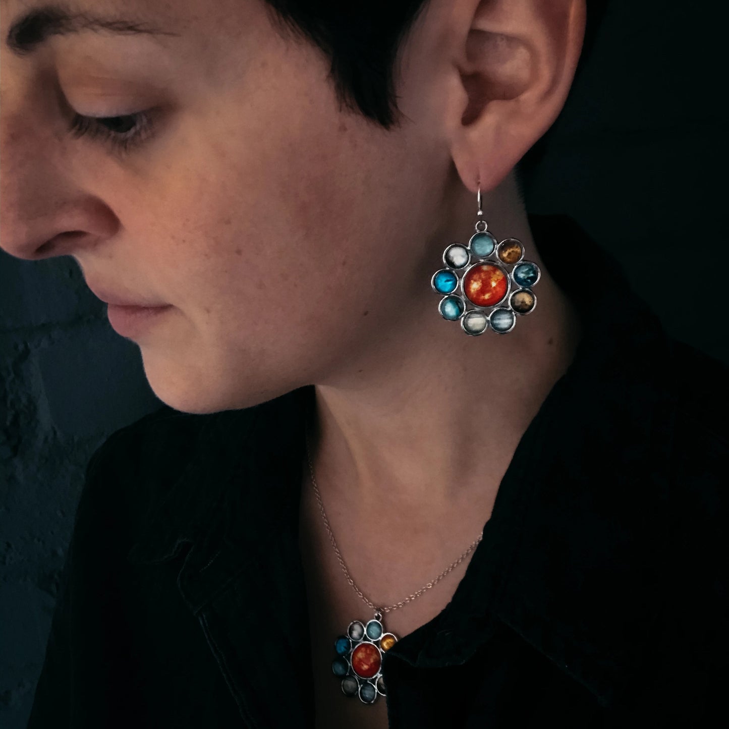 Close-up of a woman wearing colorful floral earrings with a dark background