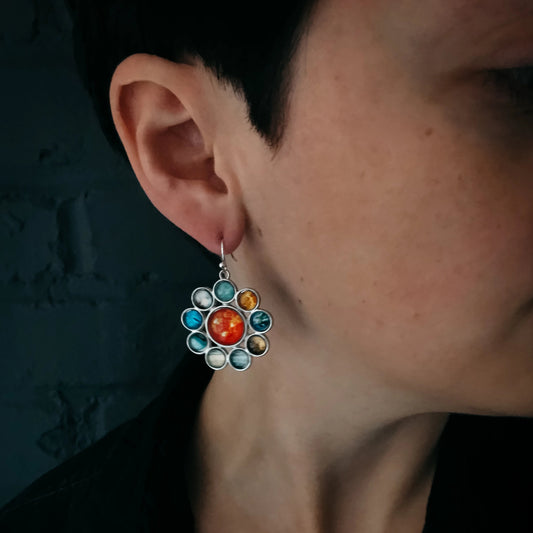 Close-up of an ear wearing a colorful floral earring against a dark background