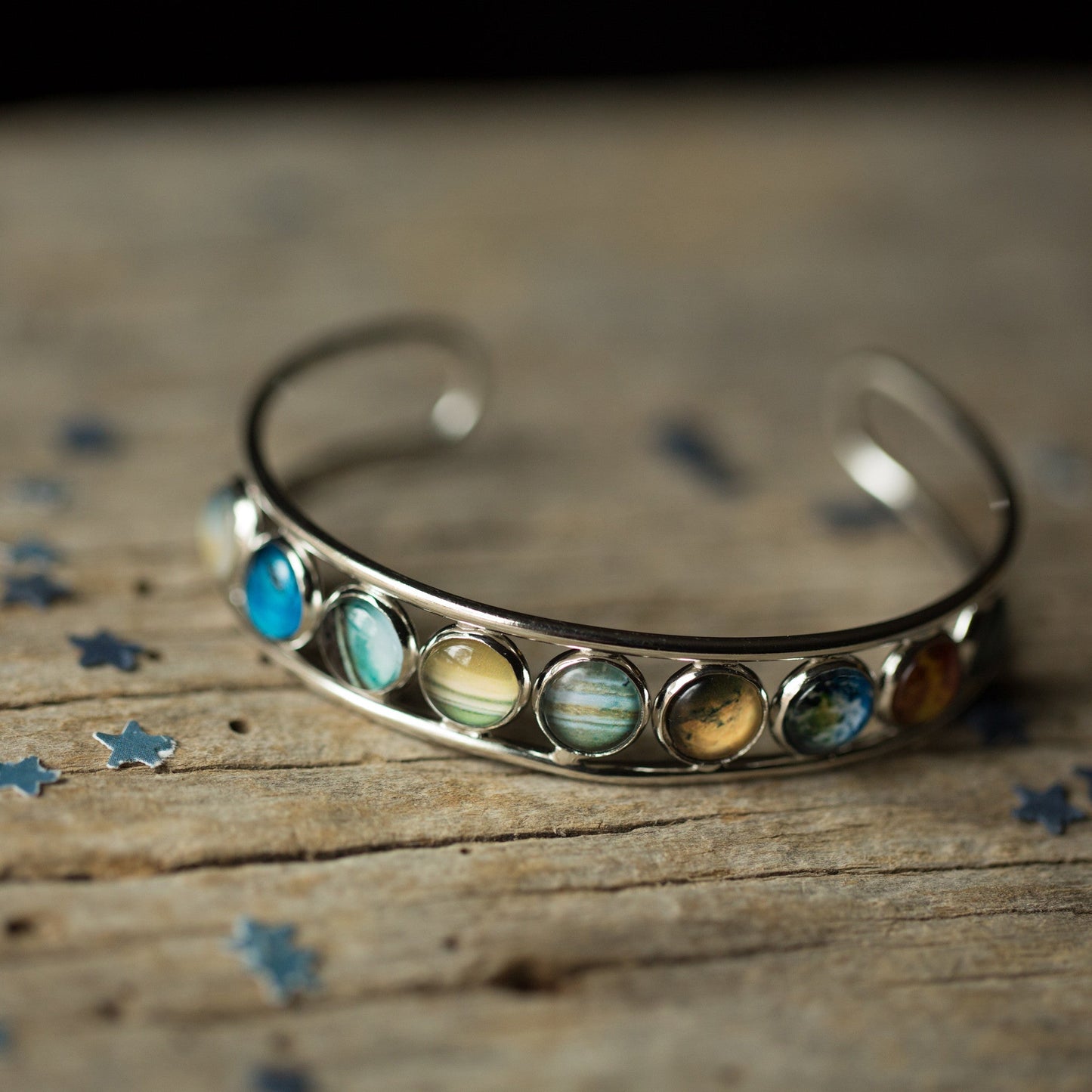 Silver bracelet with planet-like stones on a wooden surface