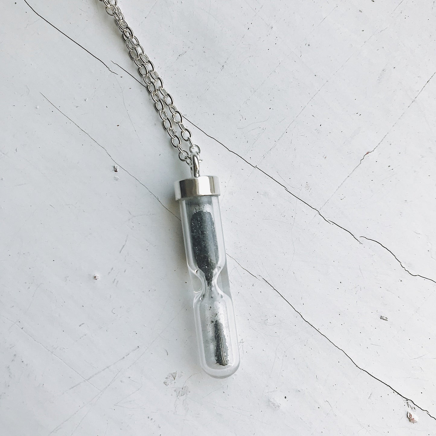 Glass vial necklace with chain on a light gray surface