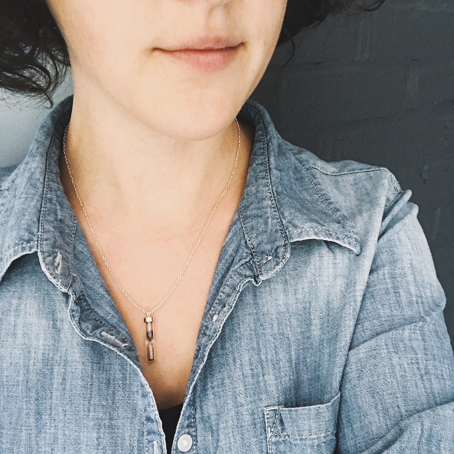 Wiman wearing a necklace with a small pendant containing meteorite dust against a dark background