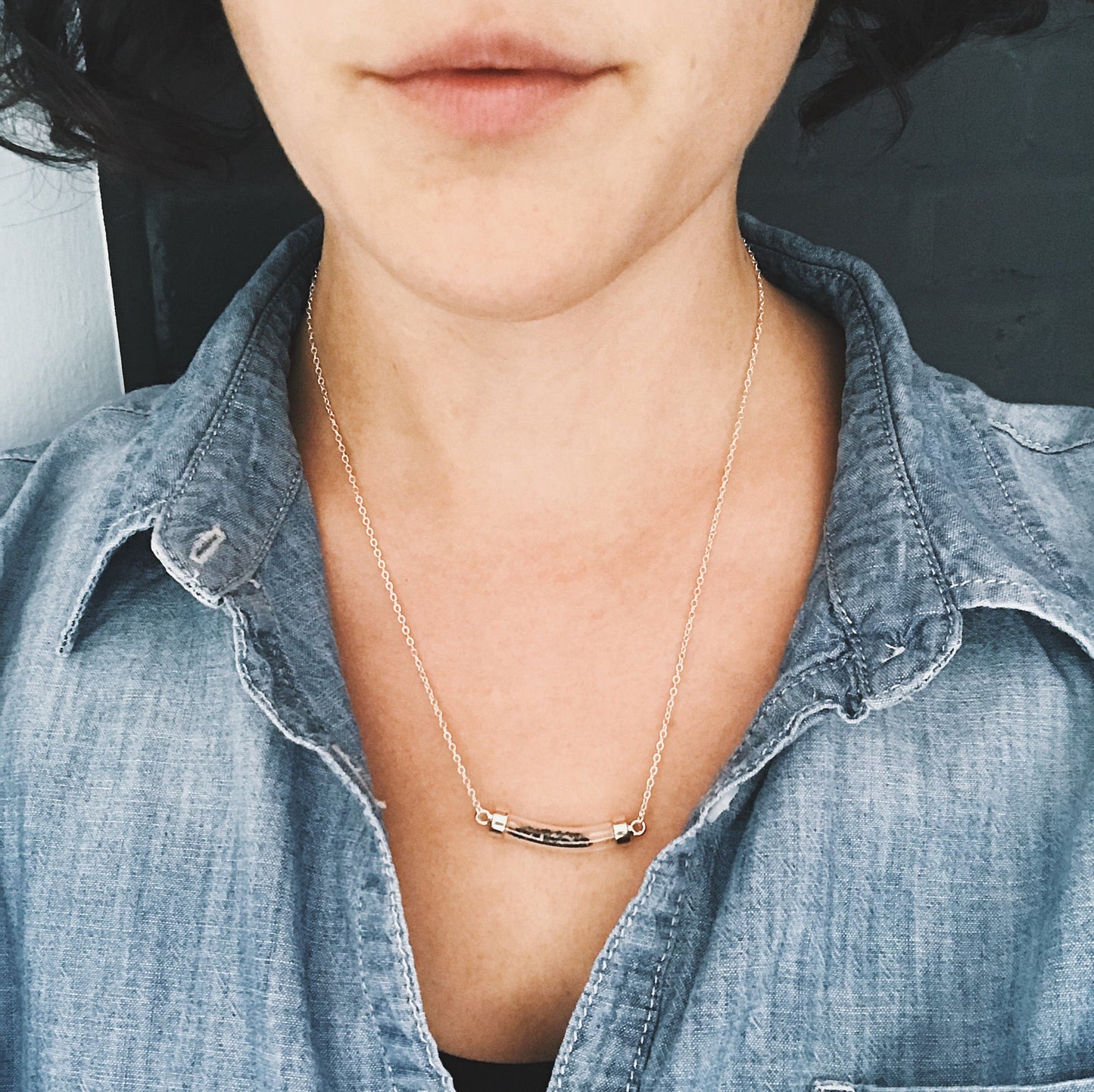 Wiman wearing a necklace with meteorite stardust with a minimalistic design, wearing a denim shirt.