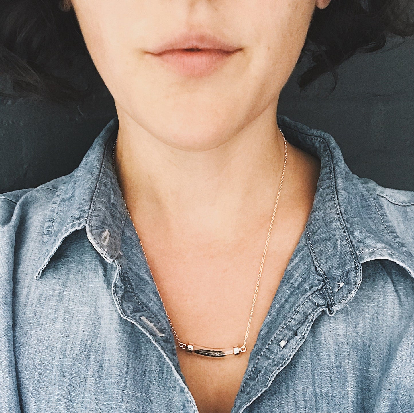Woman wearing a necklace with meteorite stardust a minimalistic design, dressed in a denim shirt.