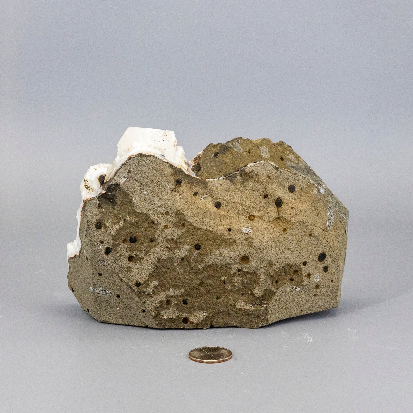 Rare chalcedony quartz cluster with apophyllite knob with a coin for scale on a gray background