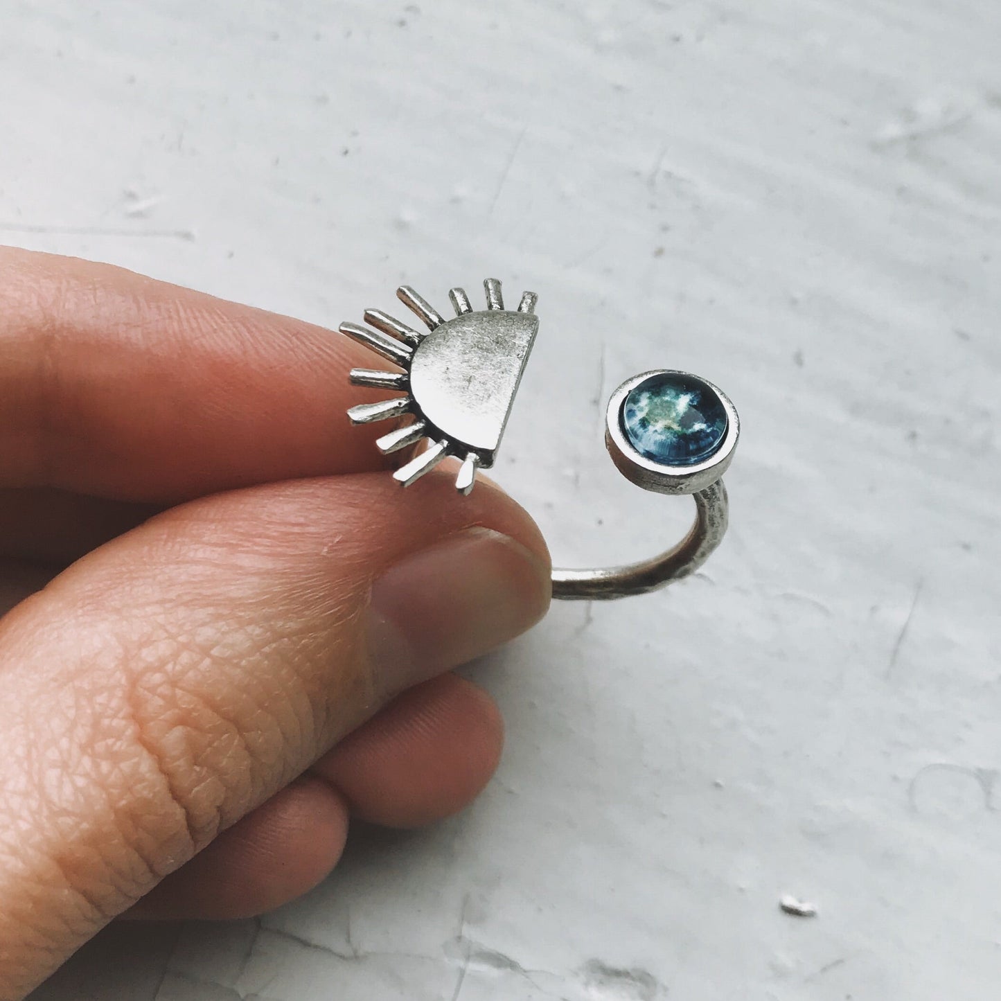 Silver ring with sun design and gemstone held by a hand on a light gray background