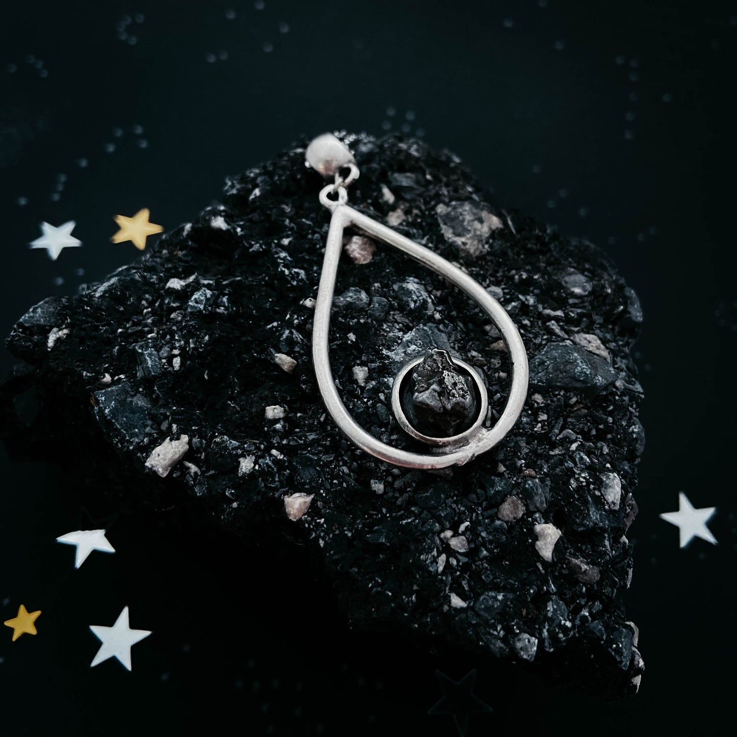 Silver teardrop-shaped pendant on a dark stone surface with decorative stars.