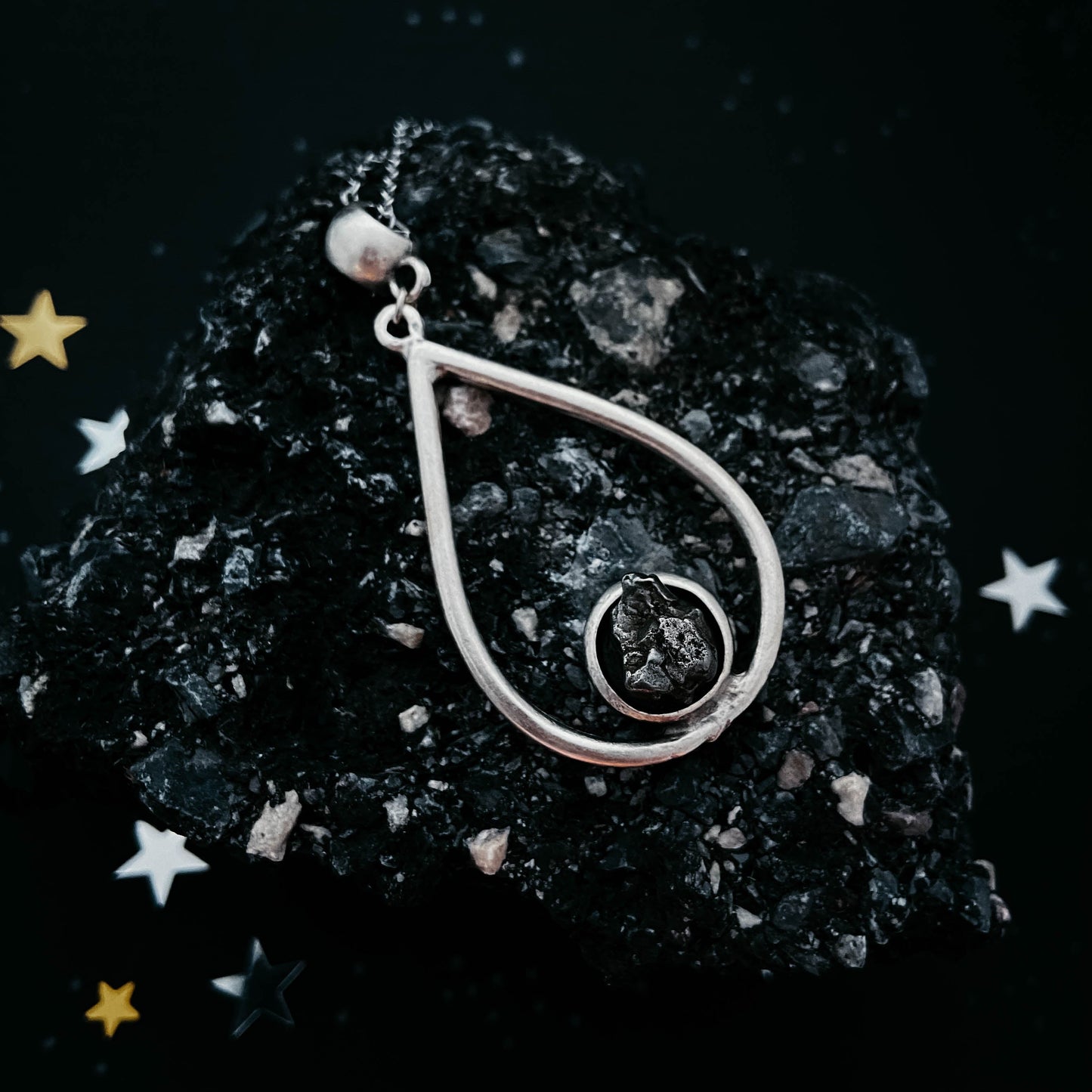 Silver pendant on a dark textured surface with stars around