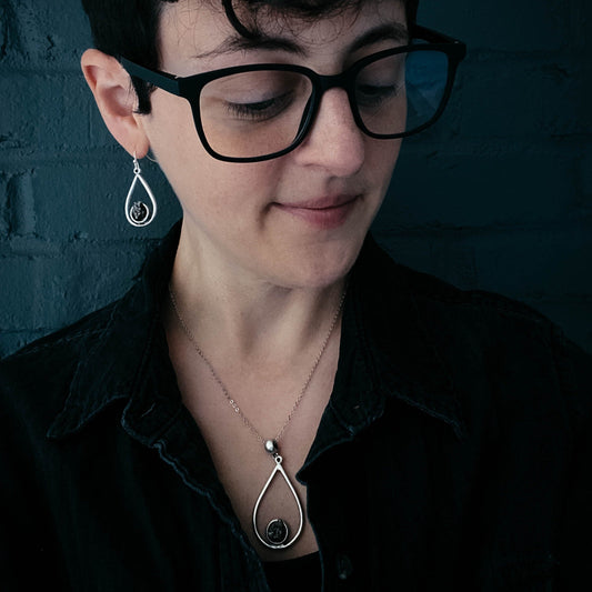 Woman wearing black glasses and a necklace with a pendant against a dark background