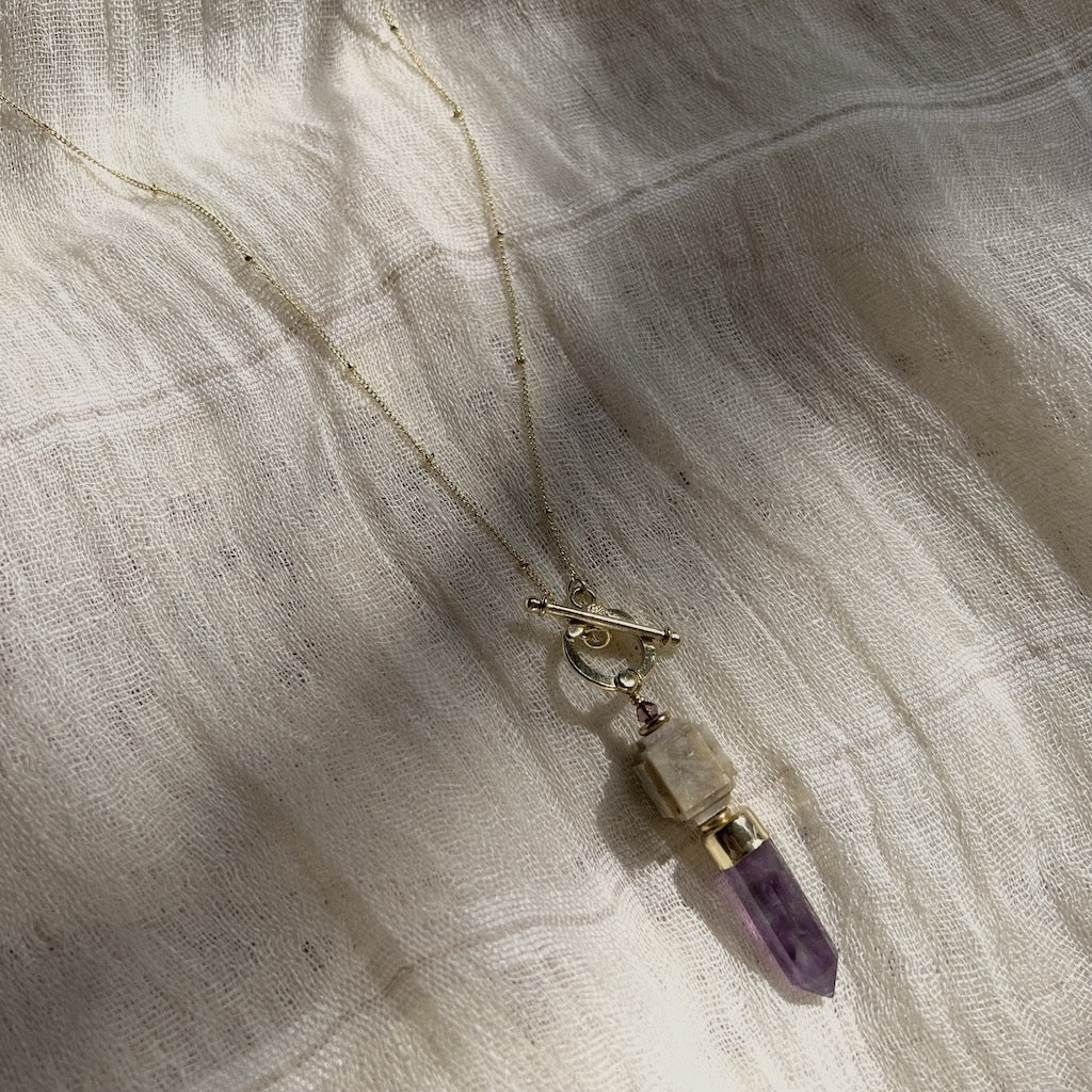 Necklace with a purple crystal pendant on a textured beige fabric background