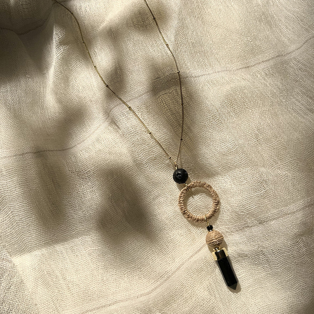 Necklace with black beads and circular pendant on a textured beige fabric background