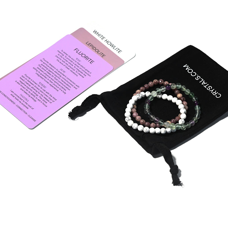 Set of three beaded bracelets on a black drawstring bag with a card next to it.