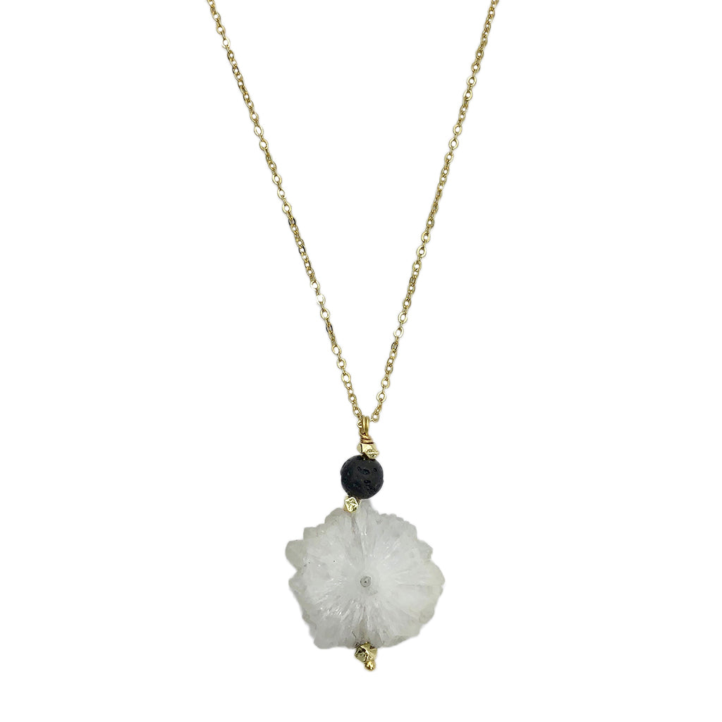 Necklace with a white floral pendant and black bead on a gold chain against a white background