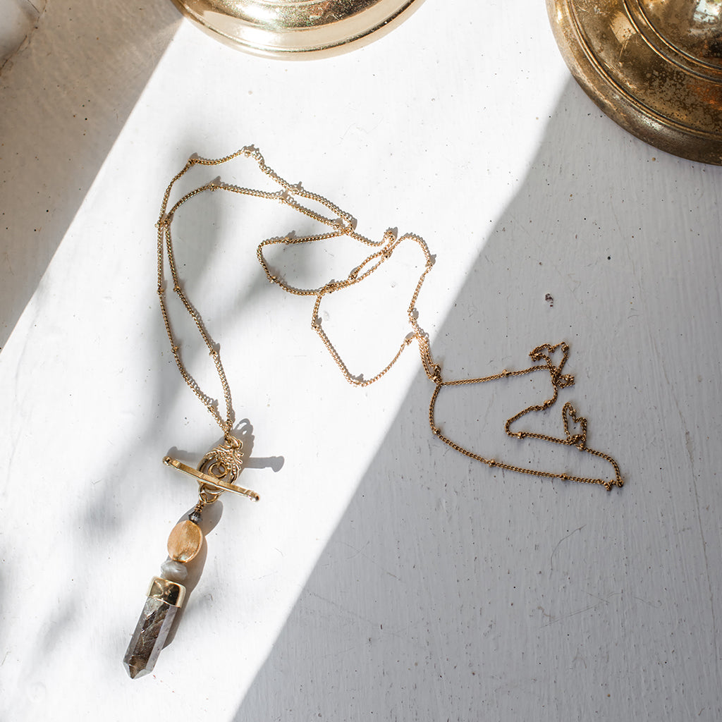Gold necklace with a labradorite pendant on a light gray surface
