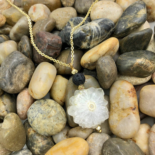 Quartz crystal necklace with a white floral pendant on pebbles