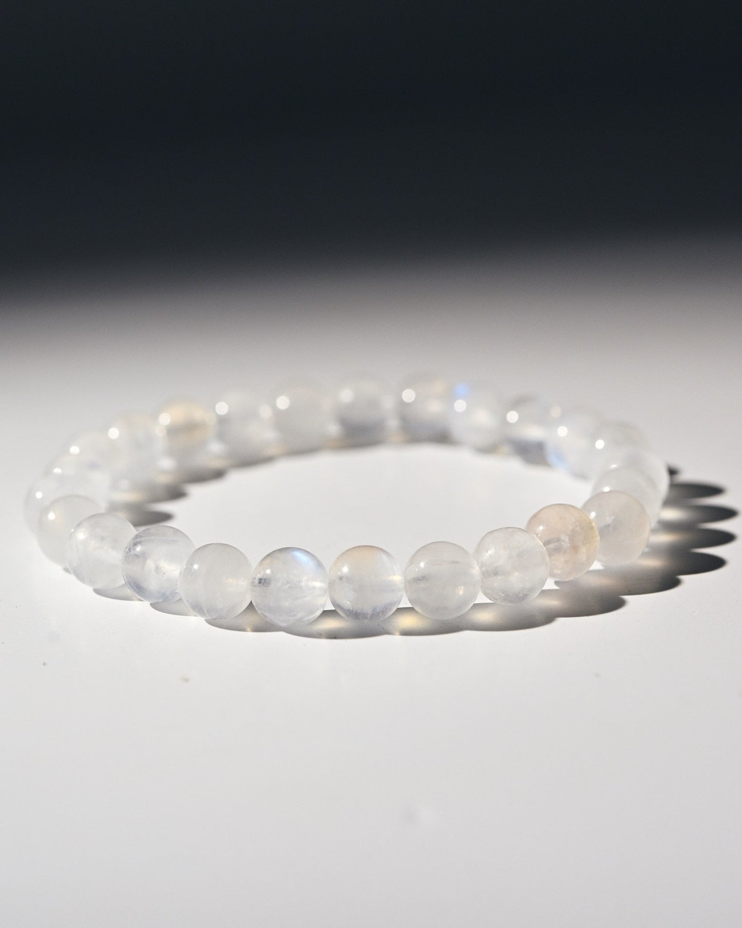 Moonstone beaded bracelet on a reflective surface with a dark background