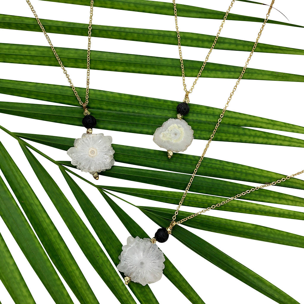 Three gold necklaces with floral quartz crystal pendants on green palm leaves