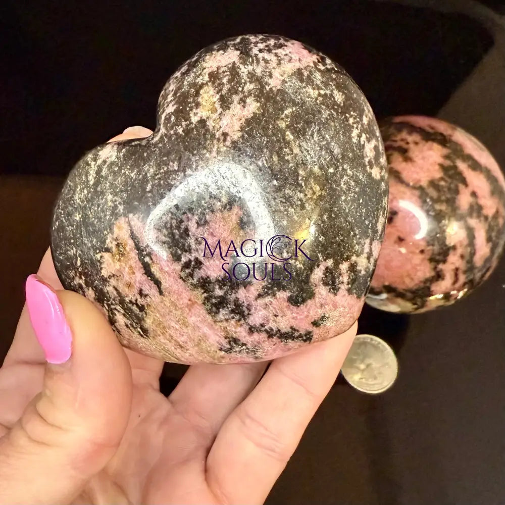 Heart-shaped rhodonite stone held by a hand with pink nail polish.