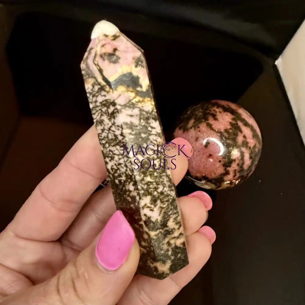 Hand holding a rhodonite crystal on a dark background