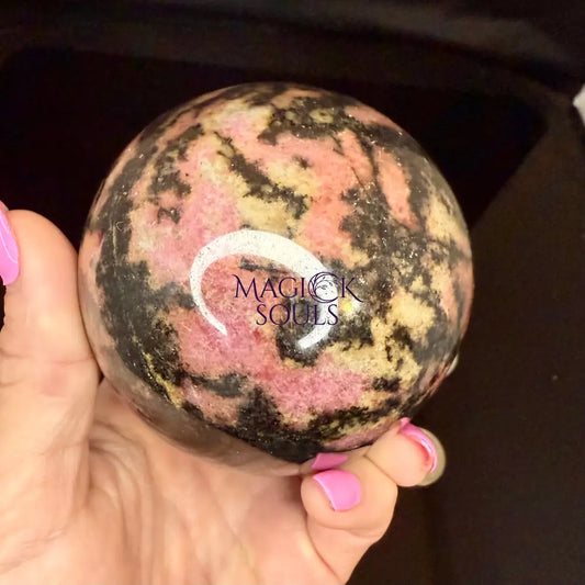 Rhodonite crystal held by a hand with pink nail polish.