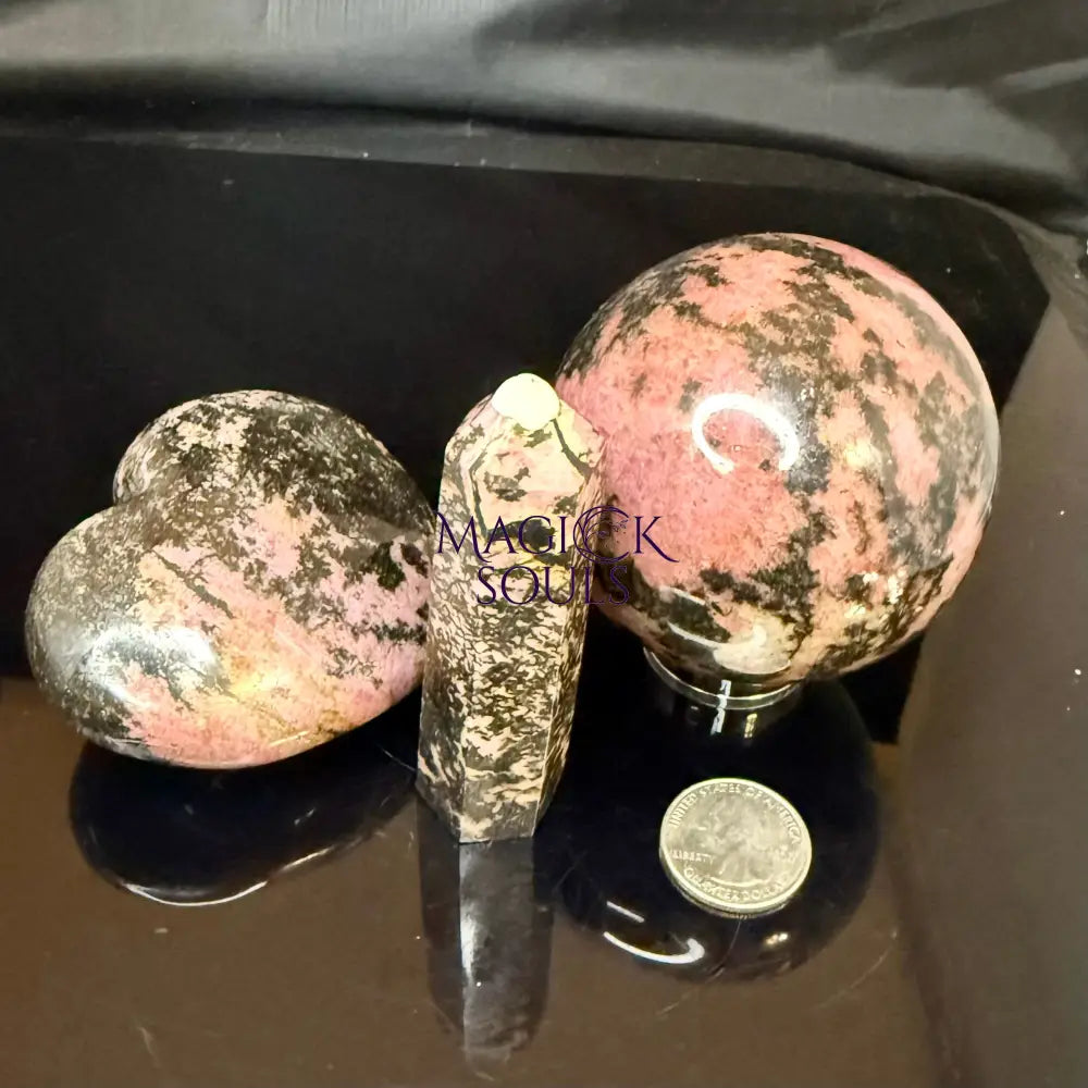 Three polished Rhodonite stone crystals on a reflective black surface.