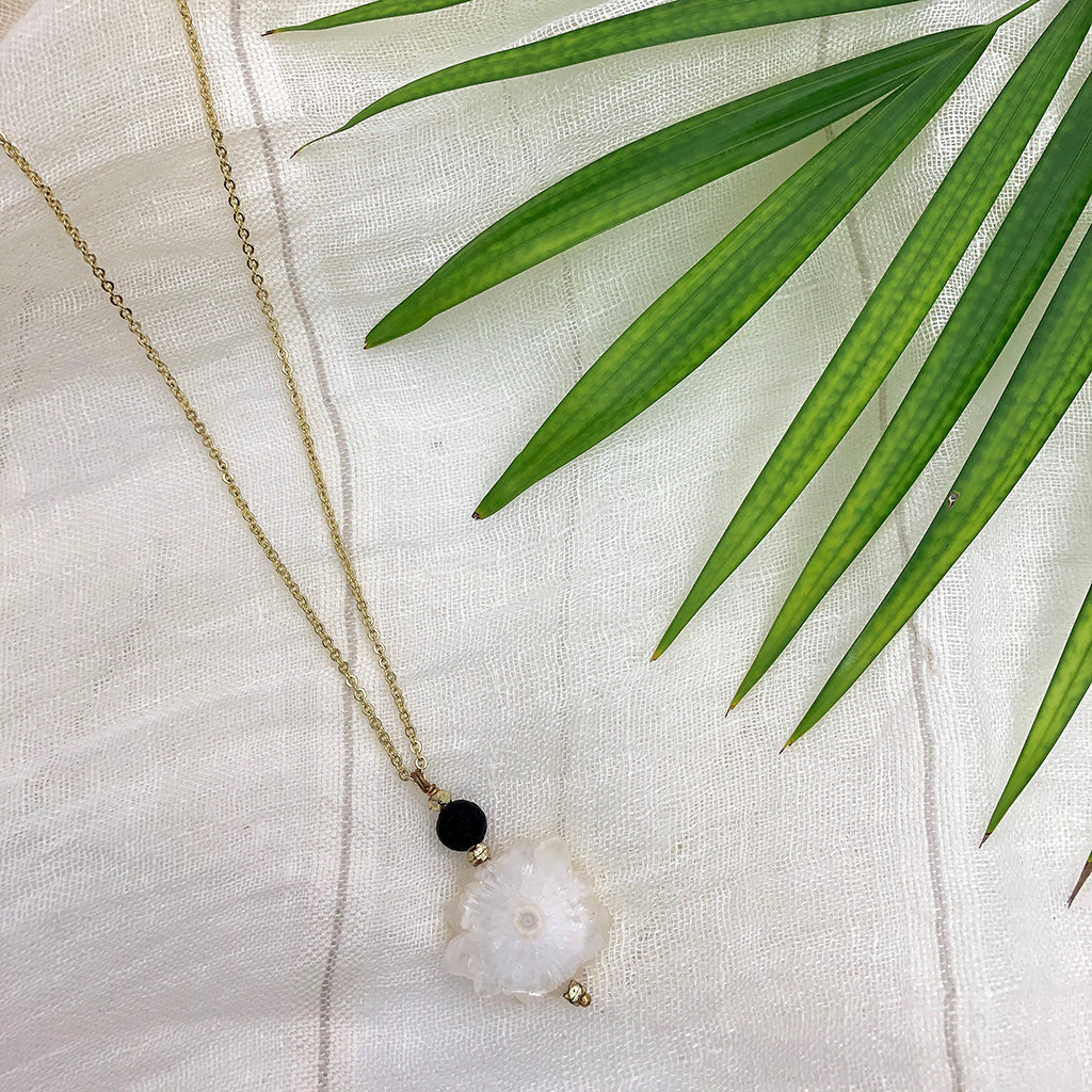 Necklace with a quartz crystal pendant and black bead on a white fabric background with green leaves.