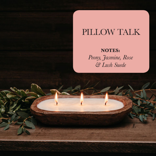 Three candles in a wooden holder with greenery on a dark background, featuring a 'Pillow Talk' product card.