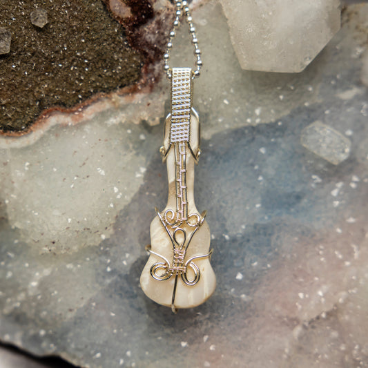 Violin-shaped agate pendant on a chain against a textured stone background