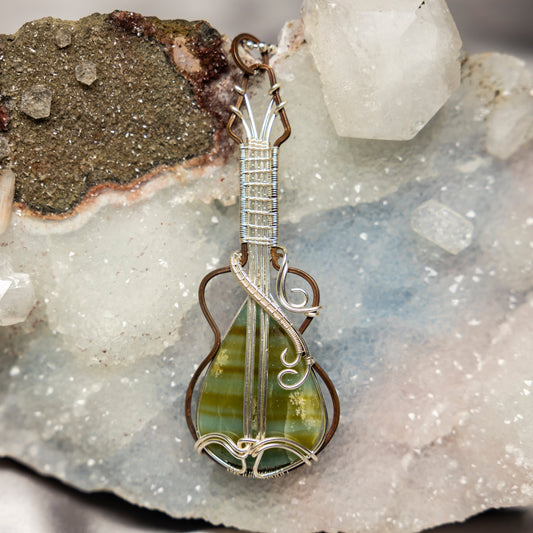 Guitar-shaped pendant with green calcite stone on a crystal background