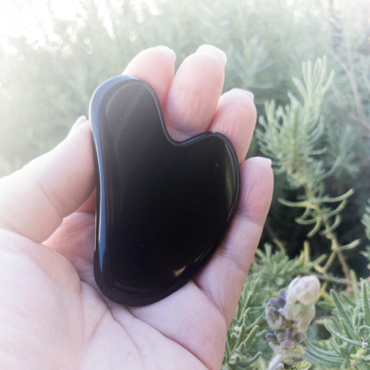 Black gua sha tool held in a hand with a natural background