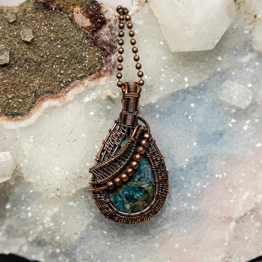 Copper wire-wrapped pendant with blue apatite stone on a crystal background
