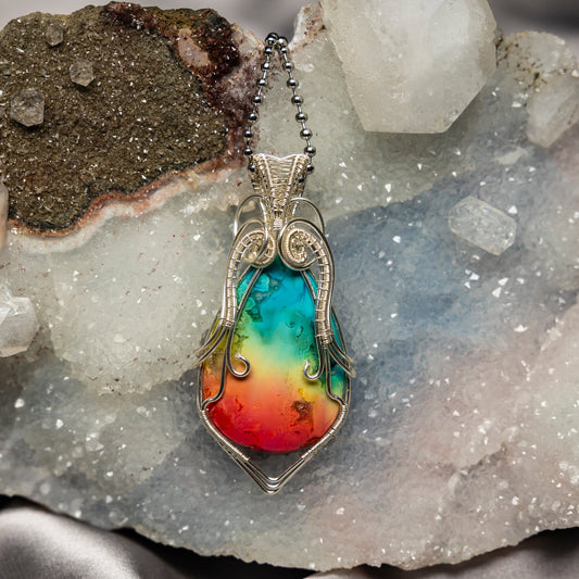Colorful chakra agate pendant with silver wire wrapping on a crystal background