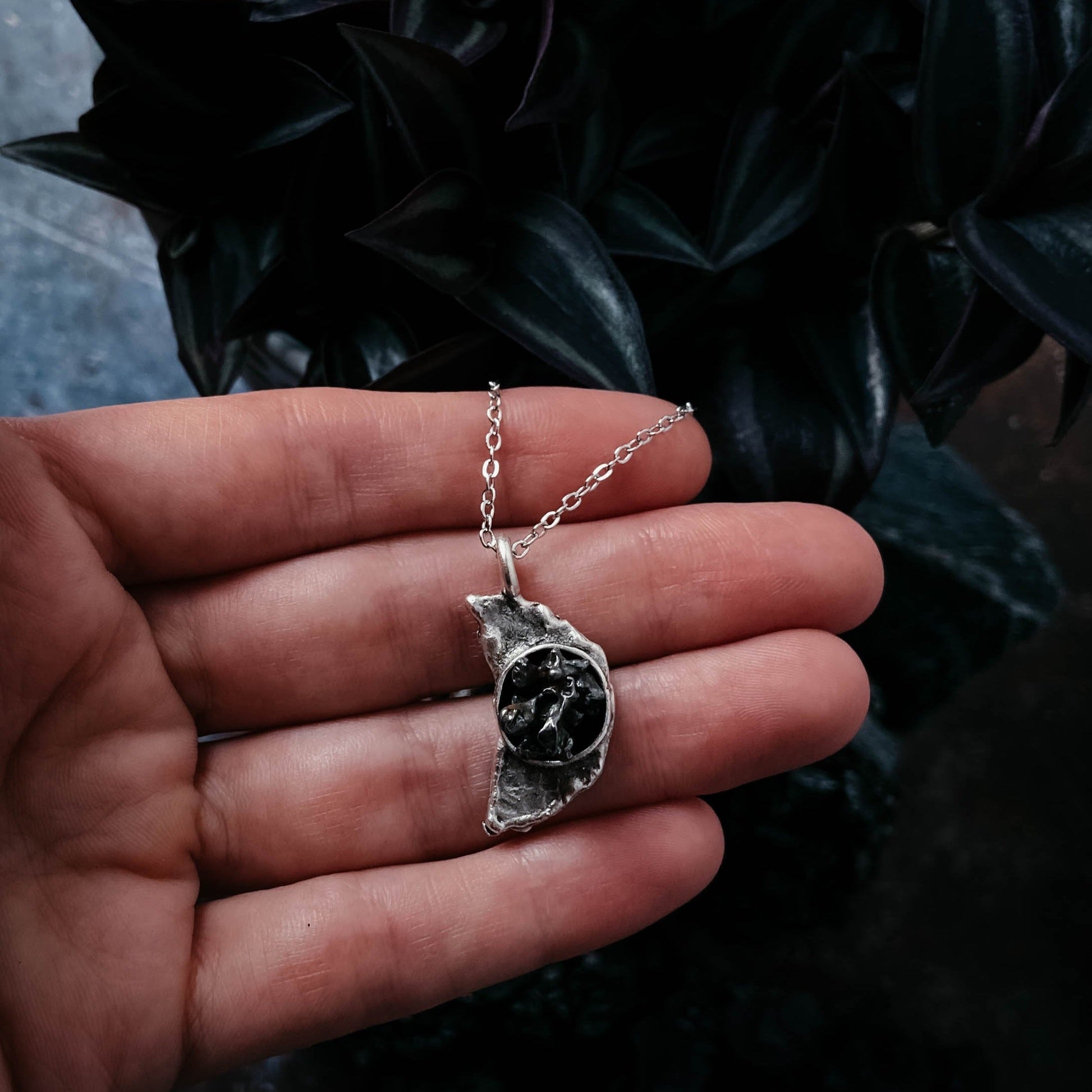 Silver necklace with a meteorite pendant held in a hand against a dark background