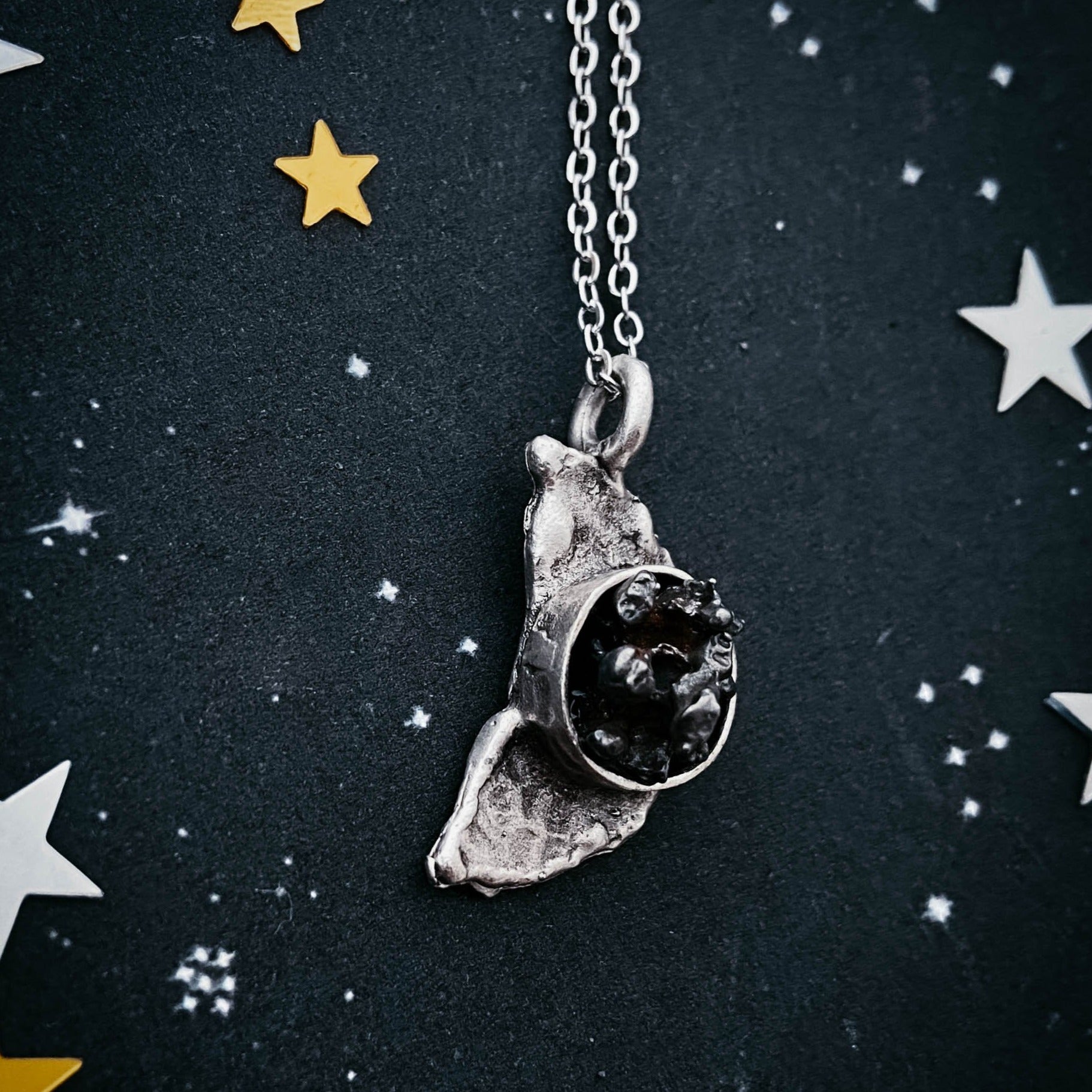 Silver necklace with a unique meteorite pendant on a dark background with star decorations