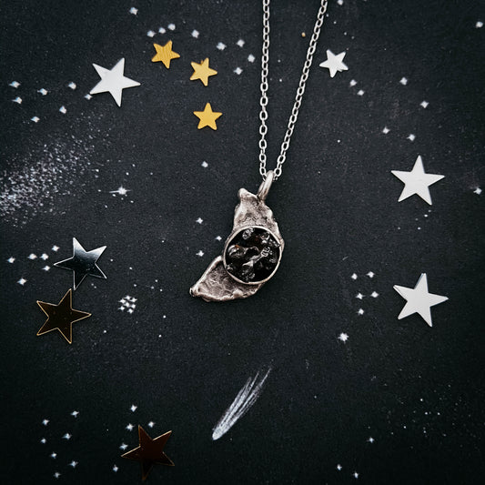 Necklace with a moon pendant with meteorite on a dark background with star decorations