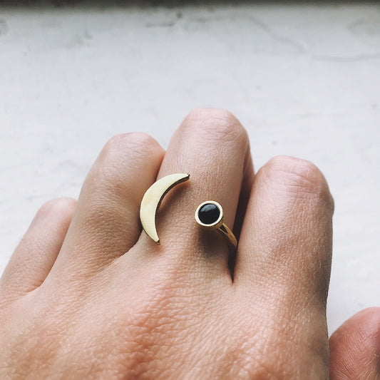 Gold ring with a black onyx gemstone on a person's finger against a neutral background