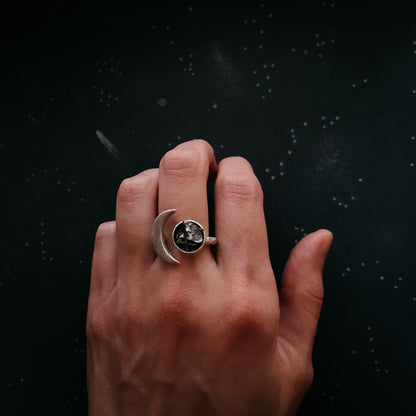 Hand wearing a silver ring with a meteorite against a dark background