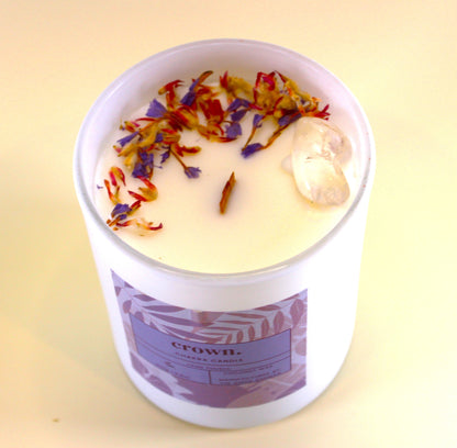 Crown chakra candle in a white container with colorful floral bits on a light yellow background